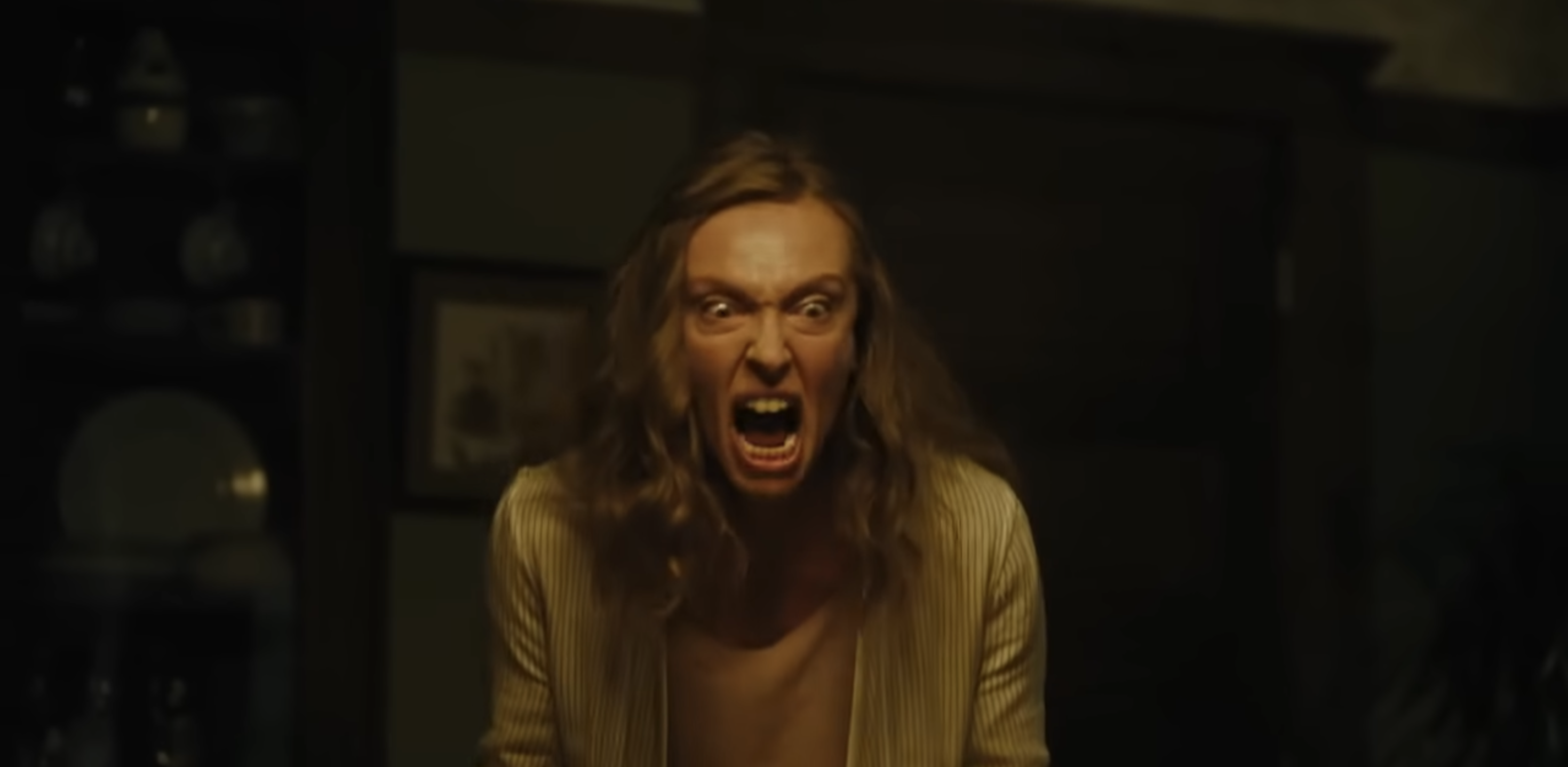 A person with long hair is indoors, expressing intense emotion with an open mouth