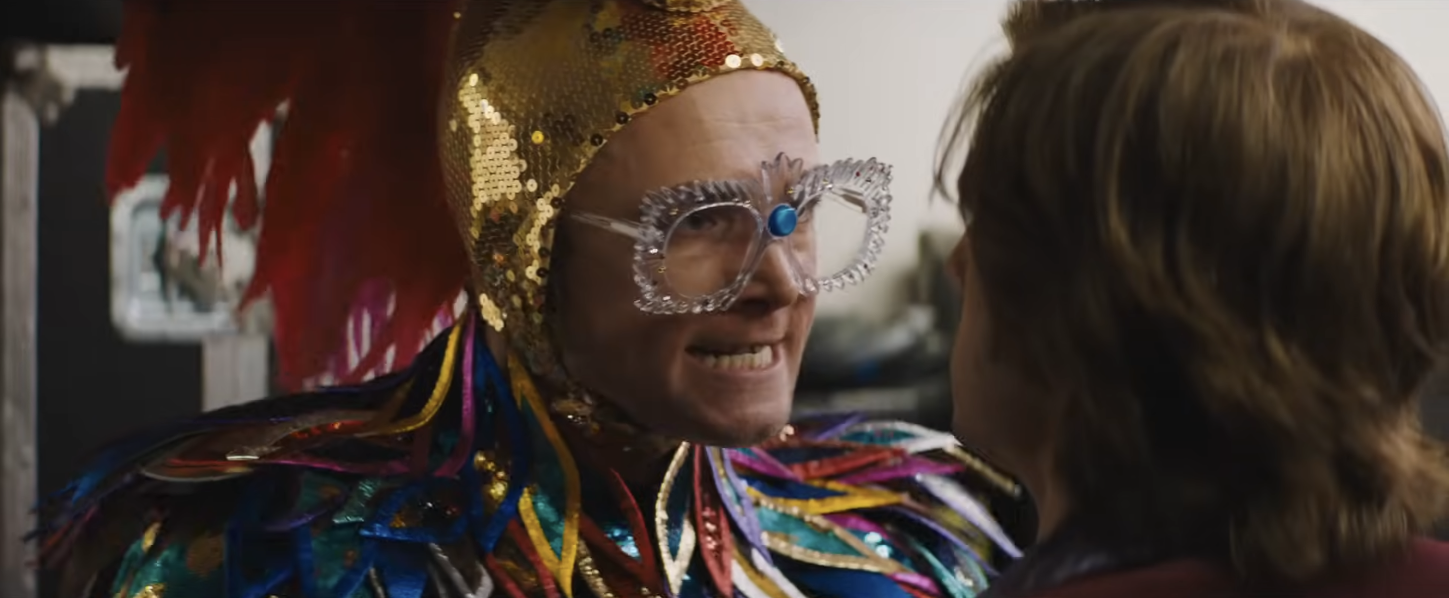 Person in extravagant feathered costume with ornate glasses, facing another person closely