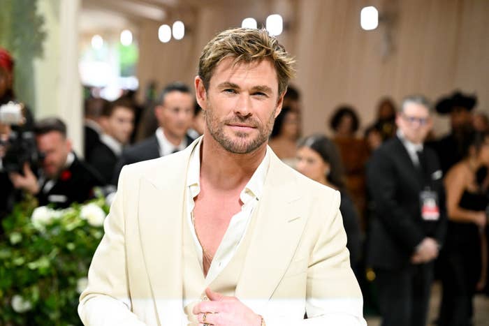 Man in an elegant light suit at a formal event, surrounded by people in evening attire