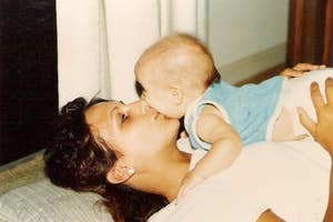 Woman lying on her back, gently holding a baby on her chest. The baby leans over to kiss her nose. Cozy, tender, parent-child moment