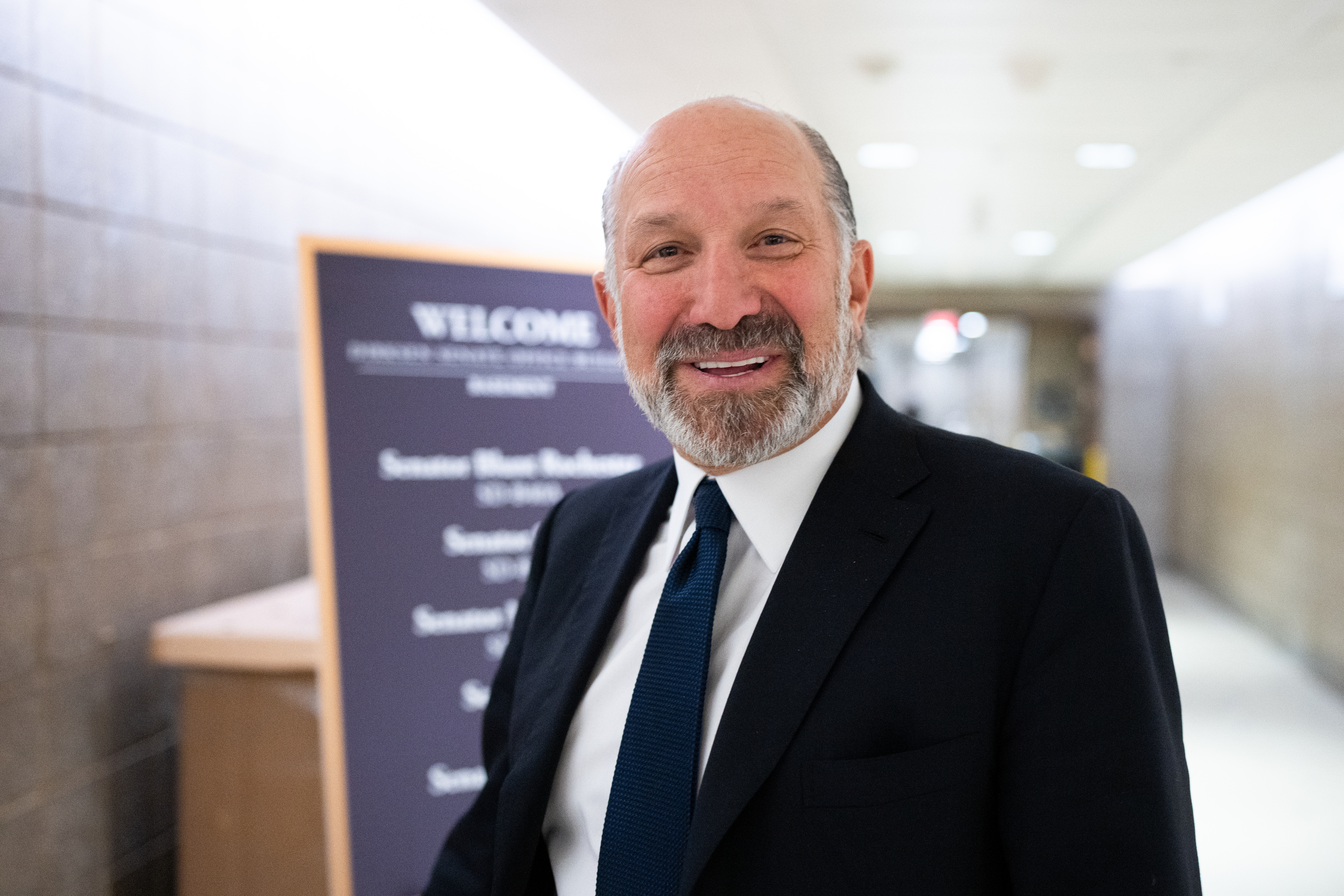 Howard Lutnick  in a suit stands in a hallway with a welcome sign in the background