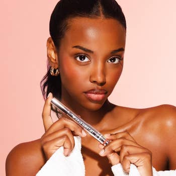 Model holding articulator liner tube, wearing hoop earrings and a achromatic robe, against a plain background