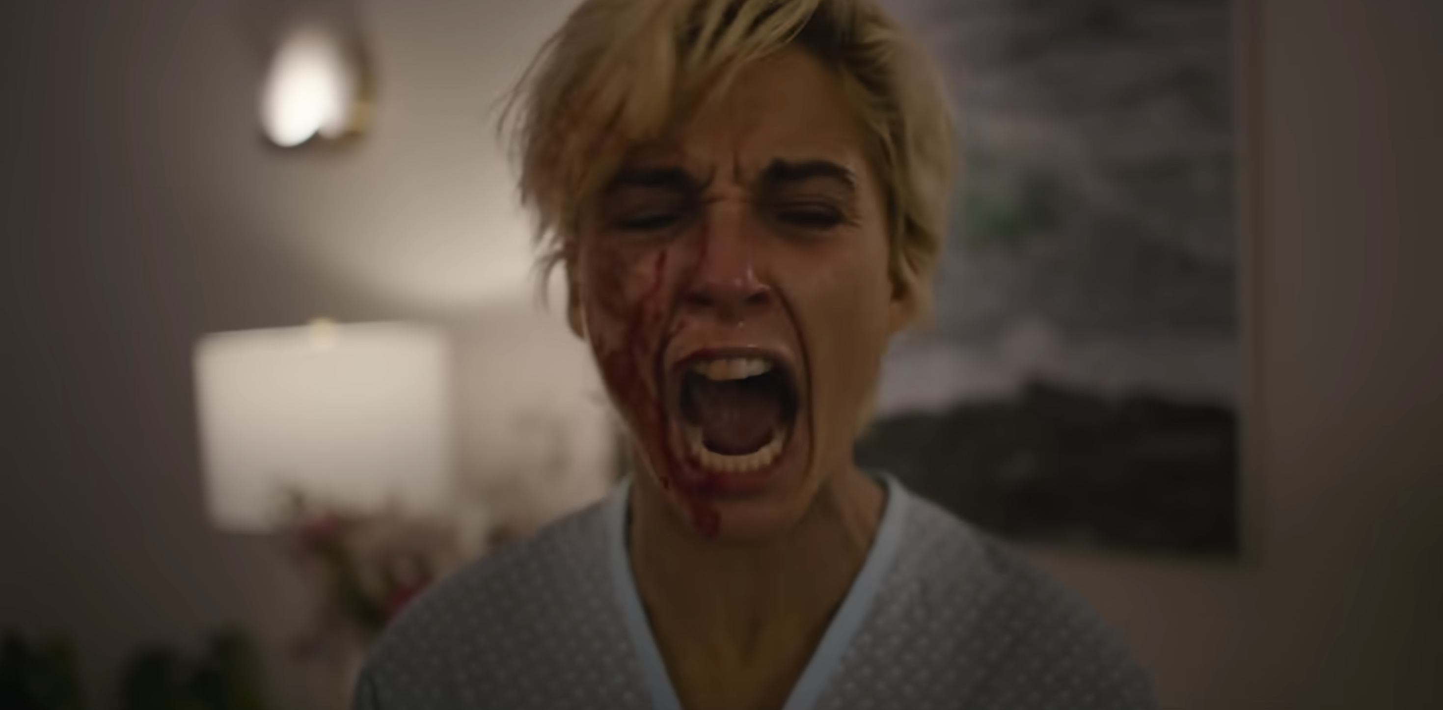 Person with short hair screaming, wearing dotted clothing. Their face is partially covered in red makeup, possibly depicting injury or trauma