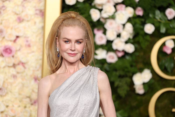 Nicole in an elegant, sleeveless gown stands in front of a floral backdrop, smiling