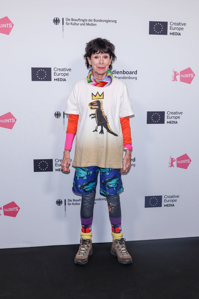 Geraldine wearing a dinosaur shirt, vibrant pants, and hiking boots on a red carpet at a Creative Europe Media event