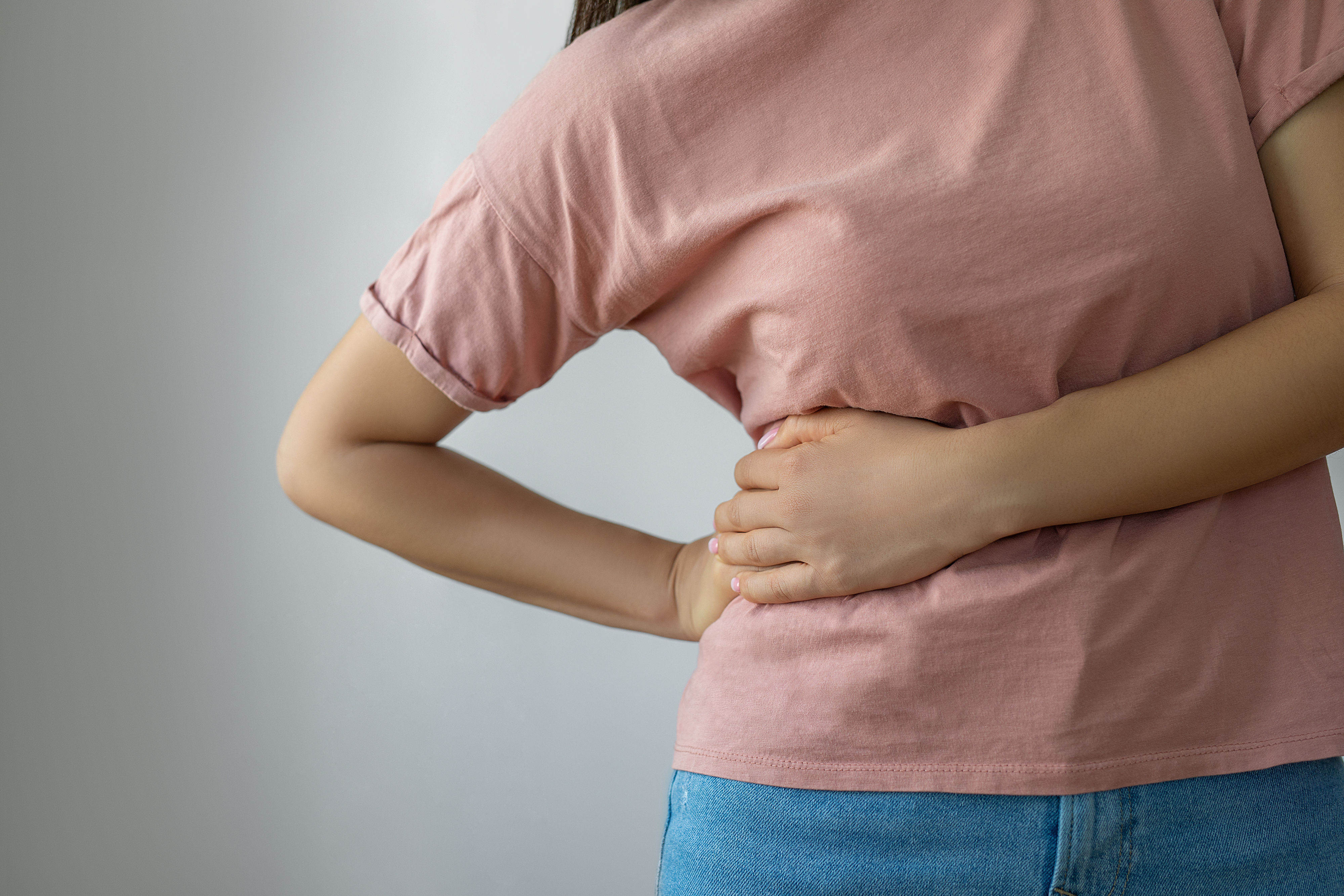 Person som holder magen, muligens indikerer ubehag eller smerte, iført en uformell t-skjorte og jeans
