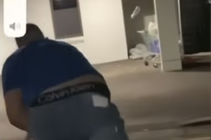 建物の前でしゃがんでいる人。スポーツカジュアルな服装が見える。背景に医療施設の看板がある。