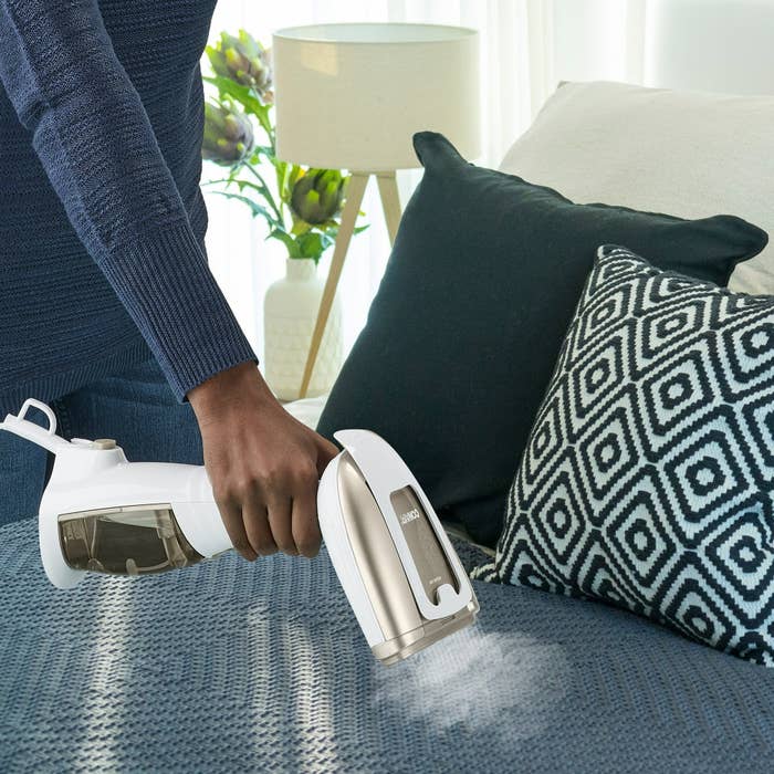 Person utilizing a handheld vacuum connected a sofa with patterned pillows successful a modern surviving country setting
