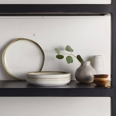 Ceramic dishes and vases displayed on a shelf; includes rounded plate, stack of plates, two vases, and small bowls. Minimalist and rustic style