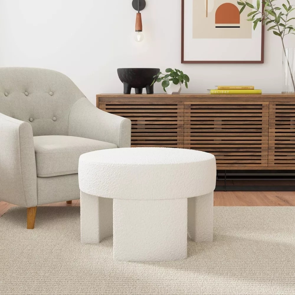 Modern living room with a beige armchair, textured round ottoman, and wooden console table with decor