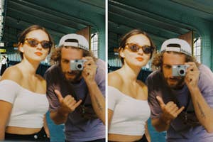 Woman in an off-shoulder top and sunglasses poses with a man taking a picture, reflected in a glass surface at a train station platform