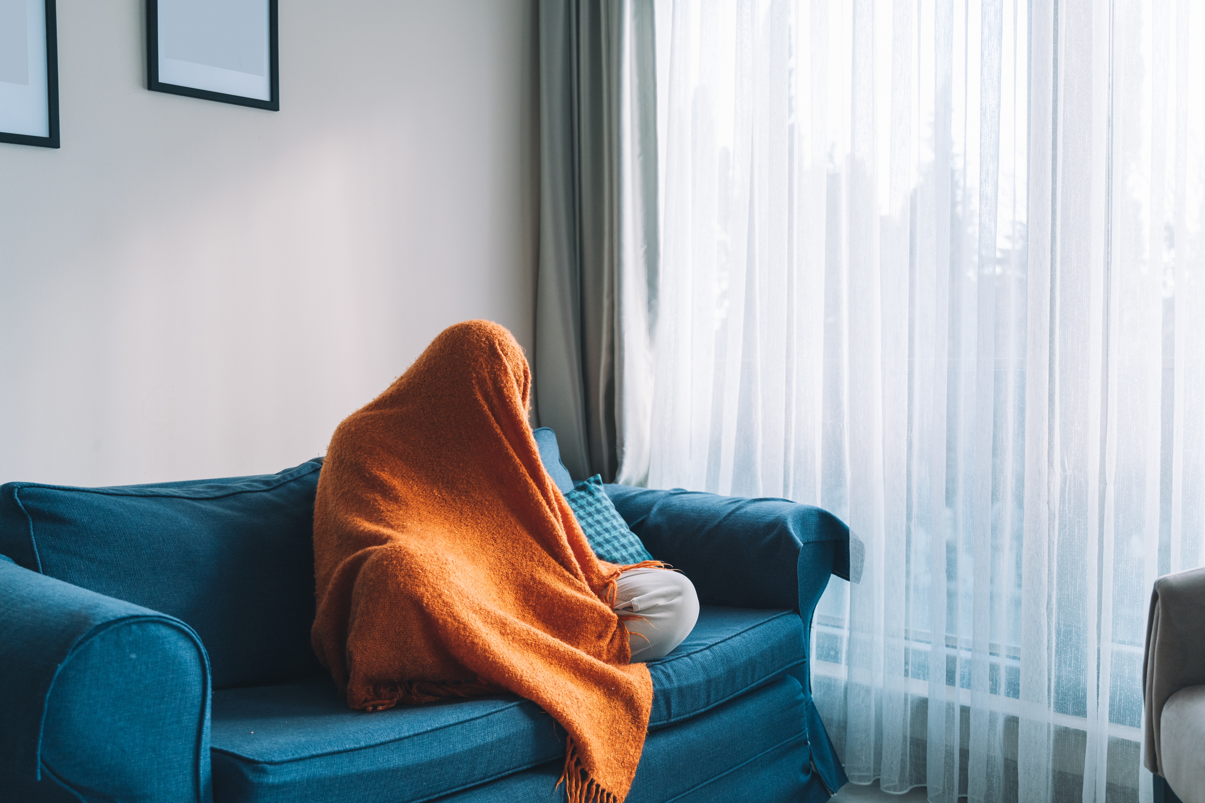 Person som sitter på en sofa med et oransje teppe drapert over dem, og skaper en koselig, avslappet atmosfære