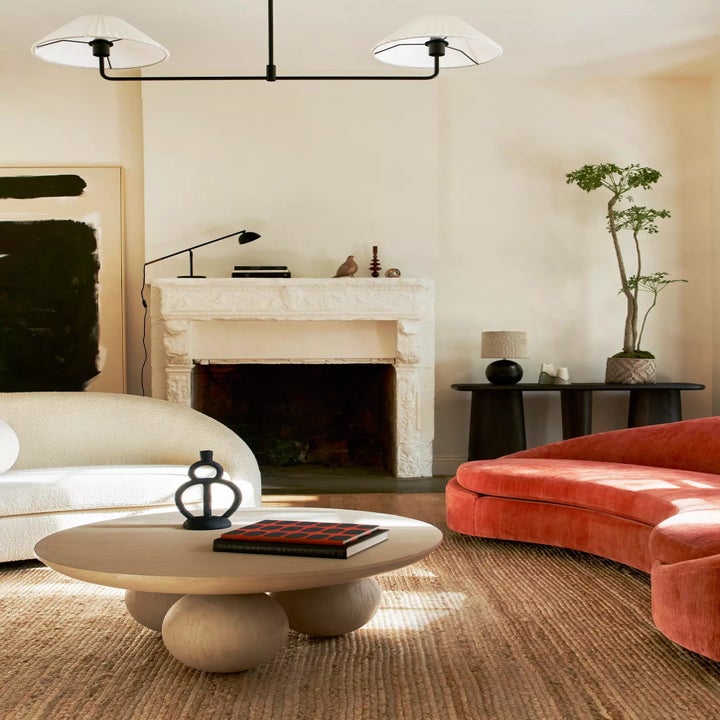 Contemporary living room with a white sofa, red velvet loveseat, round coffee table, abstract art, and a fireplace