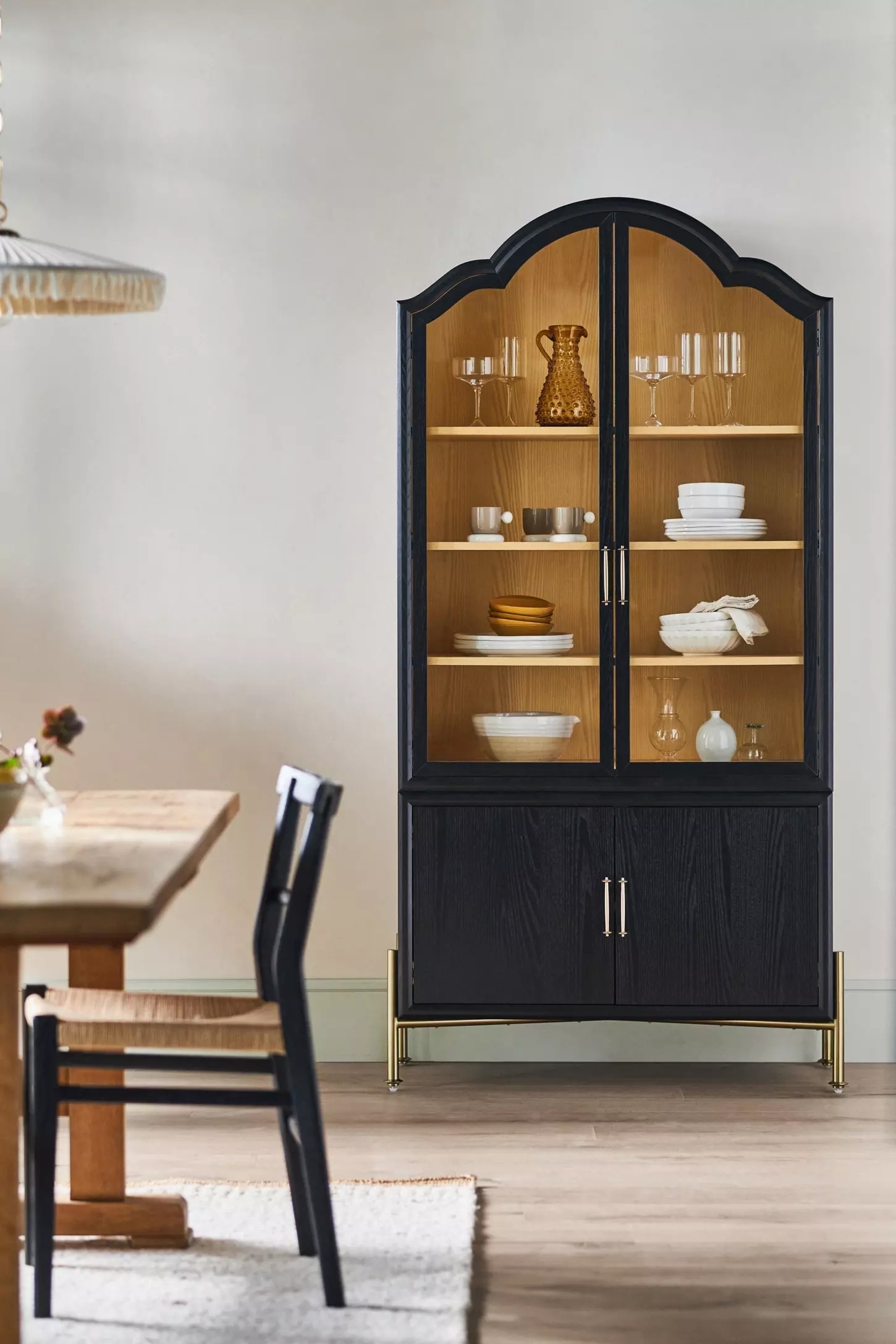 A dining room with a black cabinet displaying glassware and dishes next to a wooden table and chair