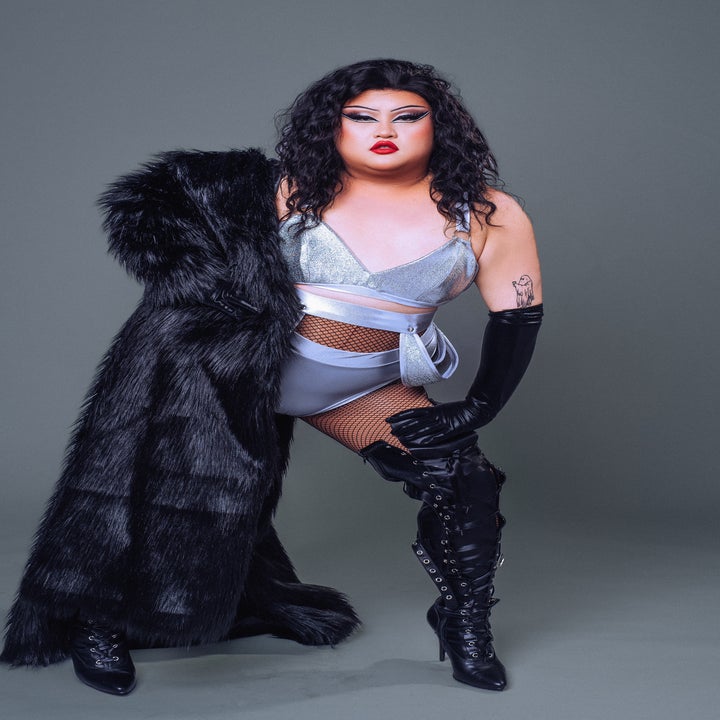 Person in glamorous outfit with a silver top, high-waisted shorts, fishnet stockings, tall black boots, and holding a black faux fur coat