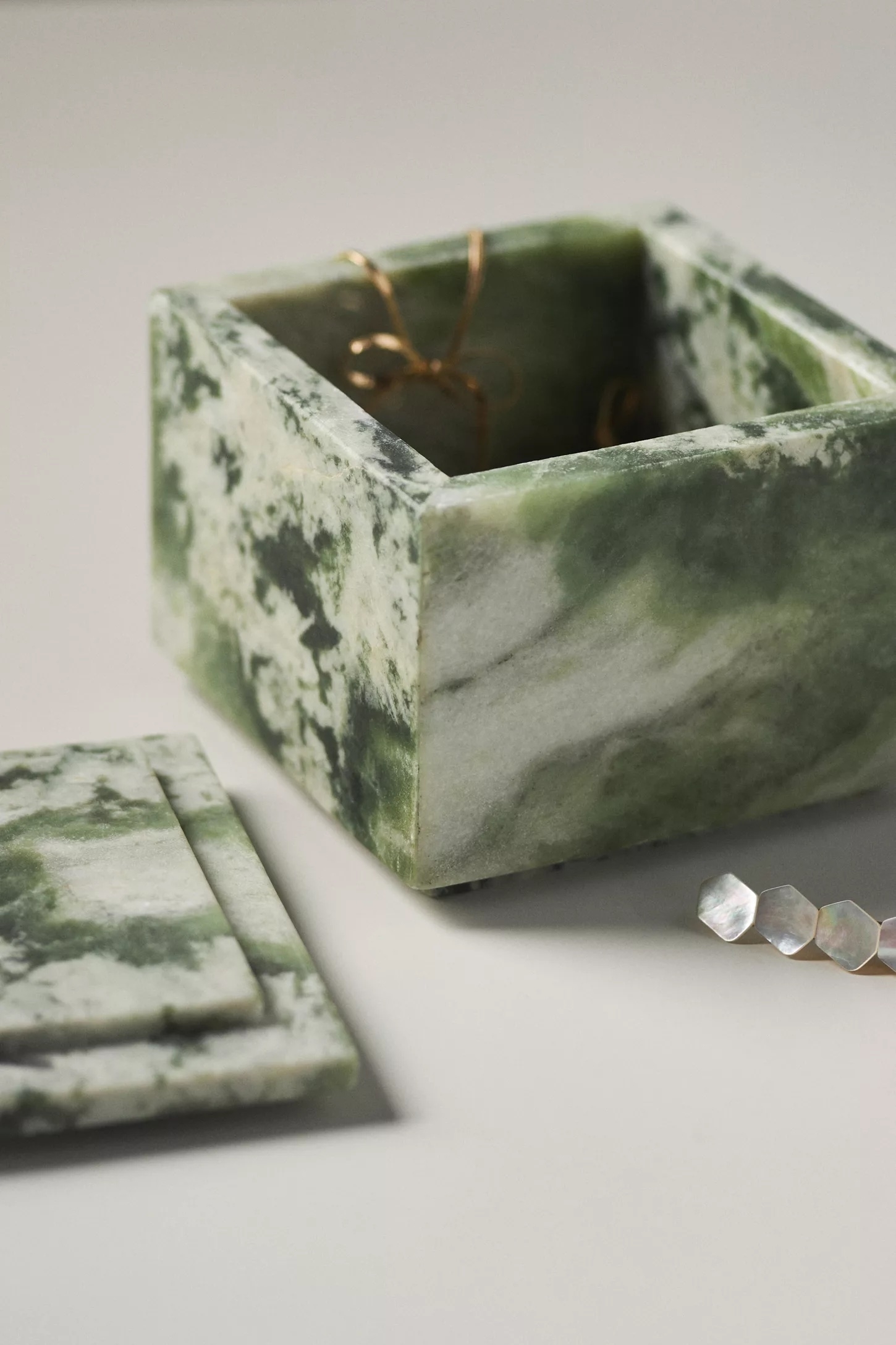 Marble-style open jewelry box with a gold bracelet inside and a closed lid nearby on a neutral background