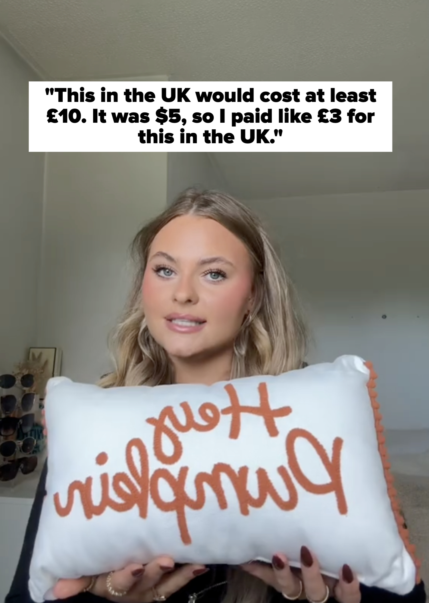 Person holding a decorative pillow with &quot;Hey Pumpkin&quot; text, smiling indoors