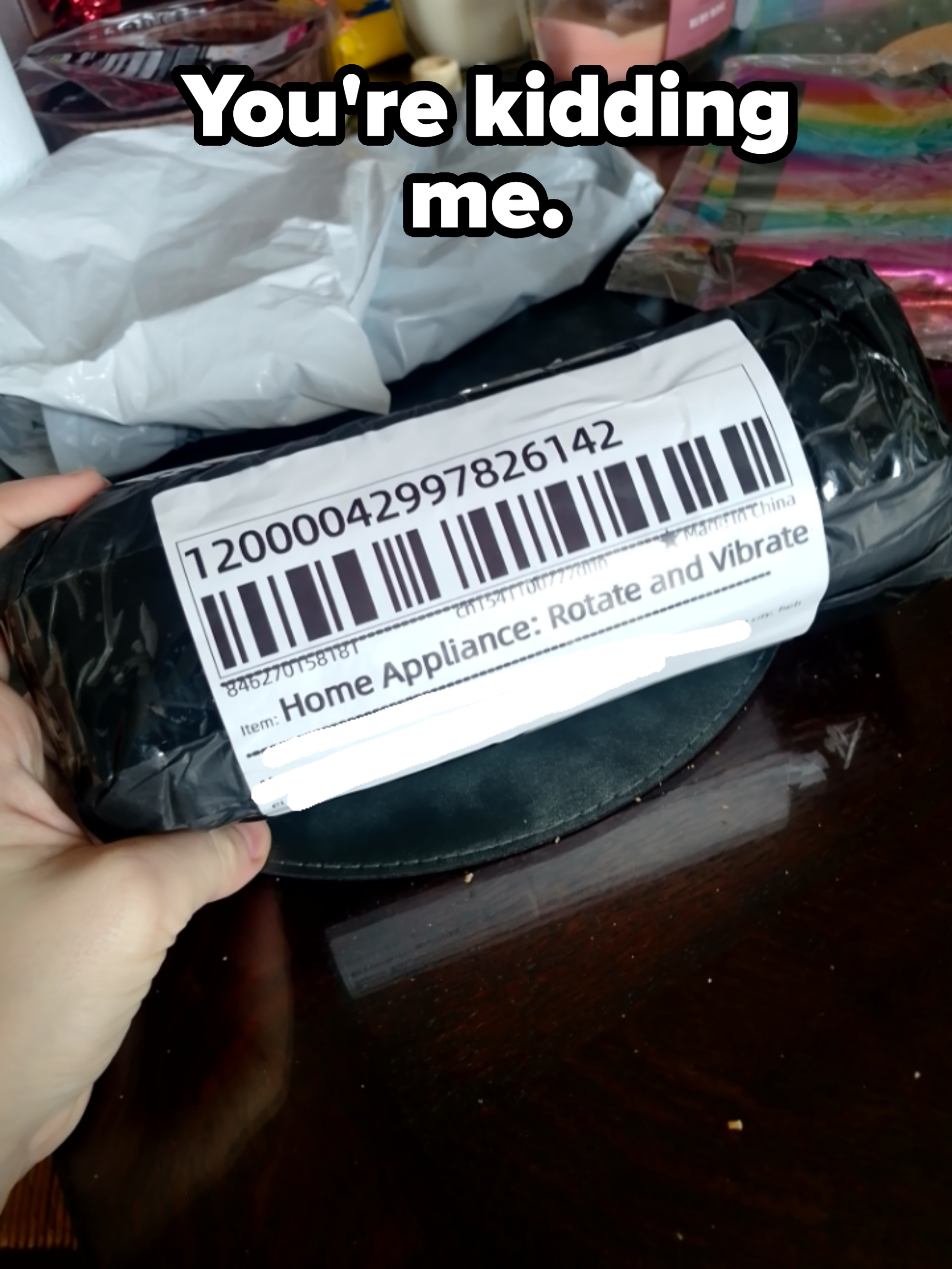 A hand holds a packaged item labeled &quot;Home Appliance: Rotate and Vibrate&quot; with a barcode visible on the packaging