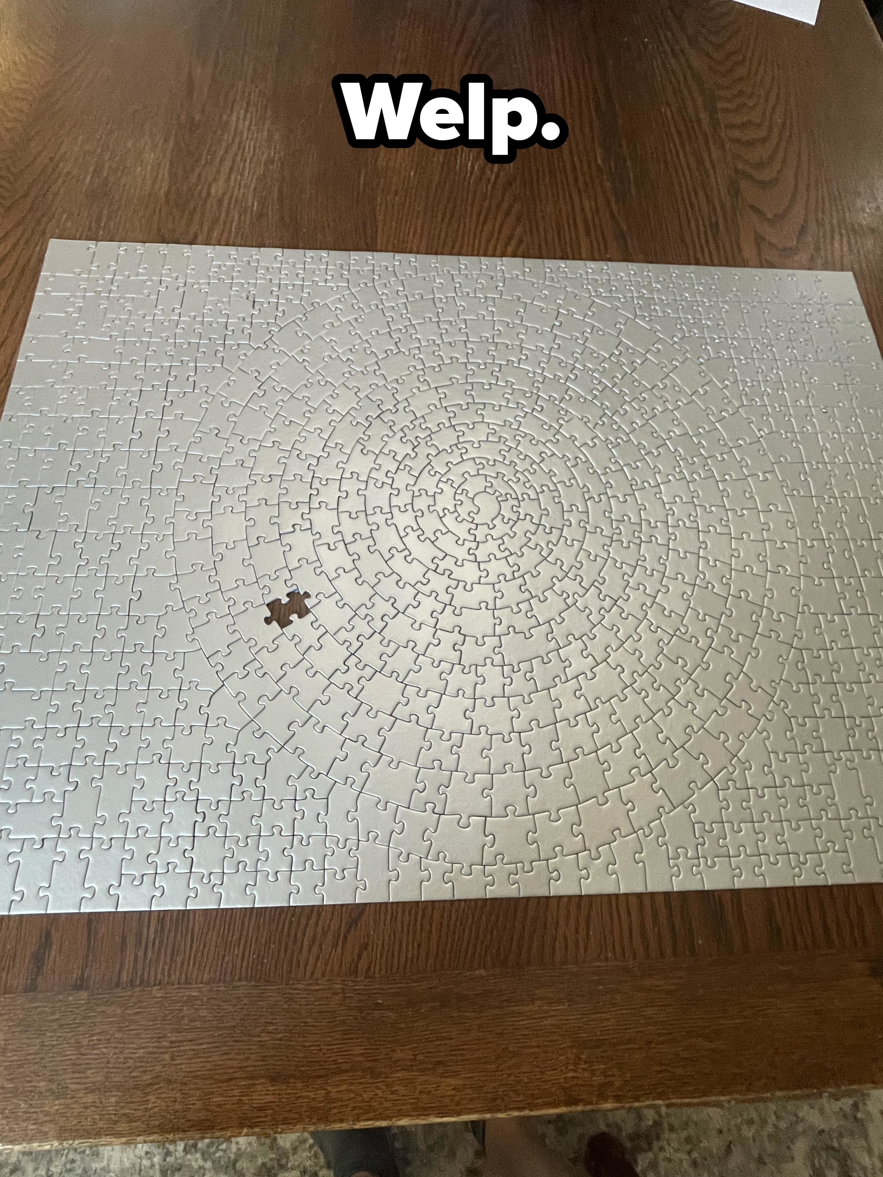 Large puzzle with spiral pattern missing one piece, placed on a wooden table