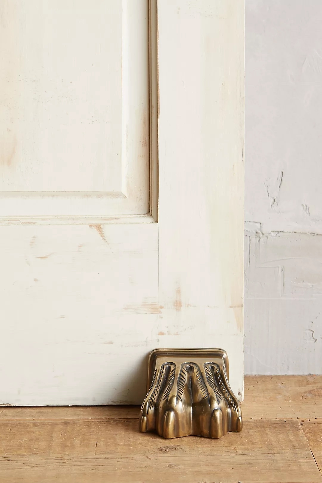 Brass claw foot doorstop holding a white door open, placed on a wooden floor, featured in shopping article