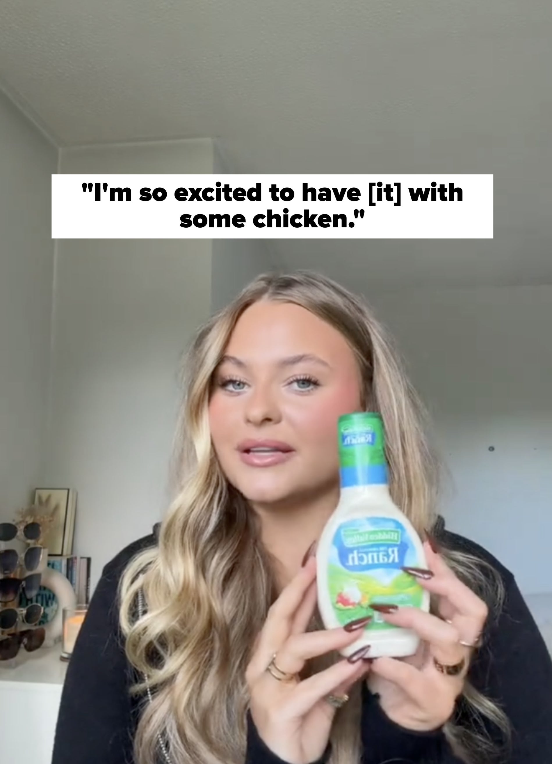 Person holding a bottle of ranch dressing in a home setting. Sunglasses hang on a rack in the background