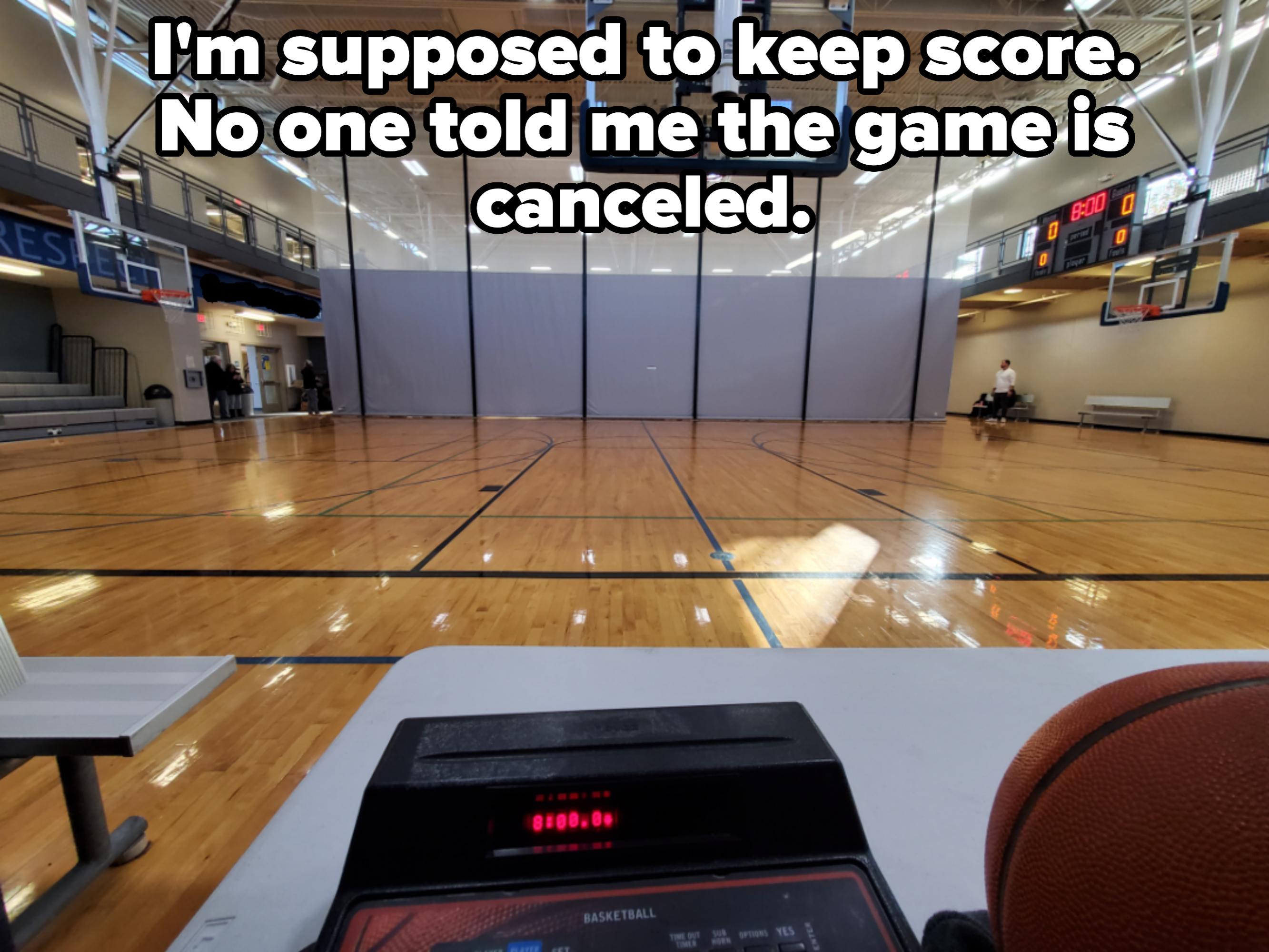 Empty indoor basketball court, viewed from the scorer&#x27;s table with scoreboard showing zeroes; basketball on the table