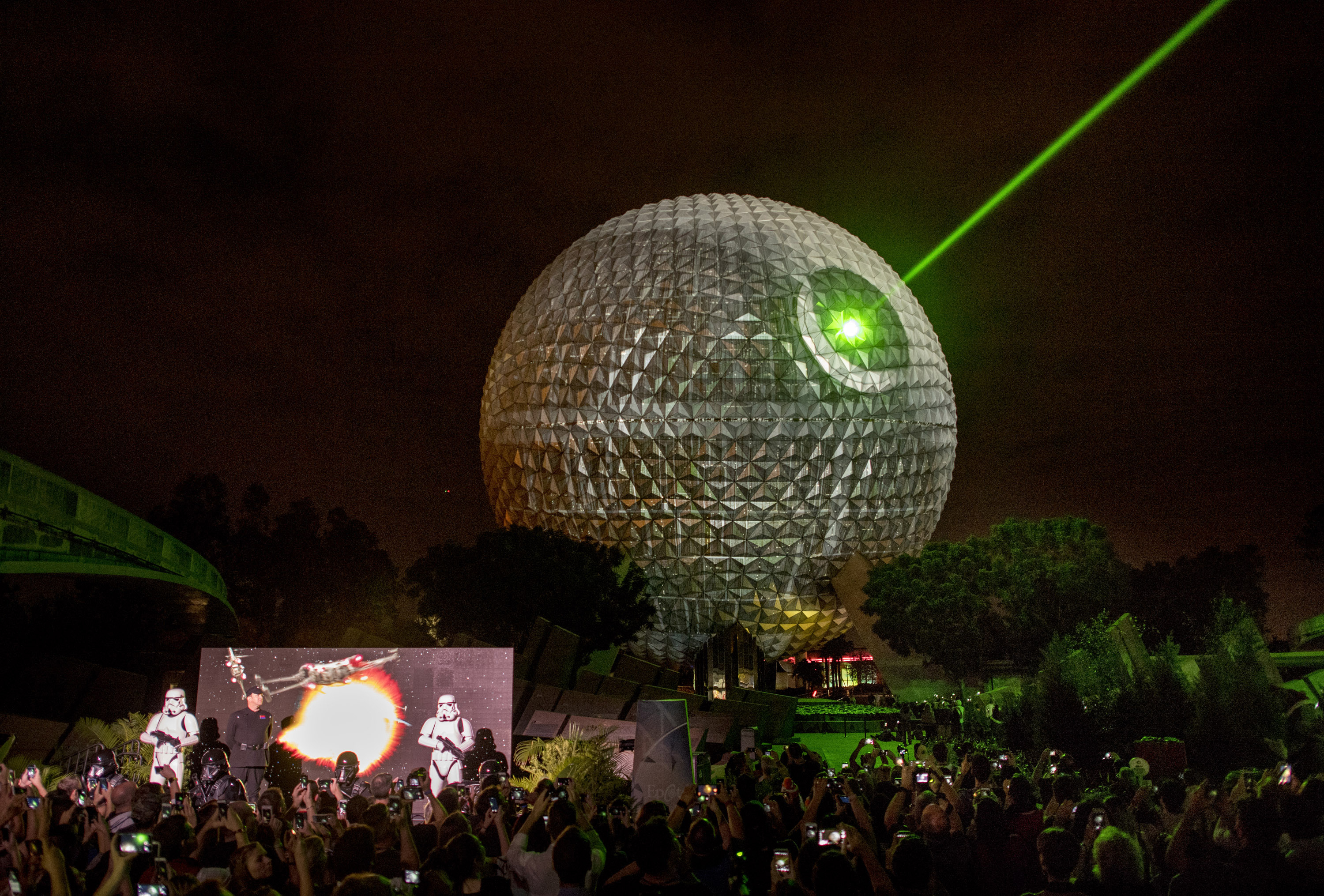 Epcot&#x27;s Spaceship Earth is lit up like the Death Star with green laser beams, surrounded by a crowd and Stormtroopers in the foreground