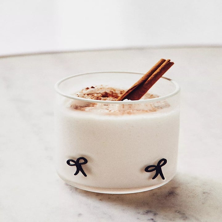 Creamy beverage in a glass with a cinnamon stick garnish and minimal bow design on a marble surface
