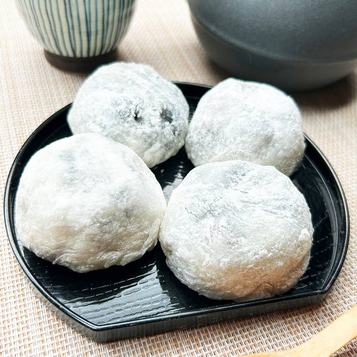 黒いお皿の上に4つの大福が並べられている。背景には湯呑みや茶碗が見える。