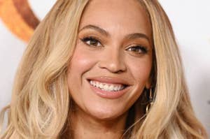 Person with wavy hair smiling in a close-up portrait, wearing subtle makeup and hoop earrings