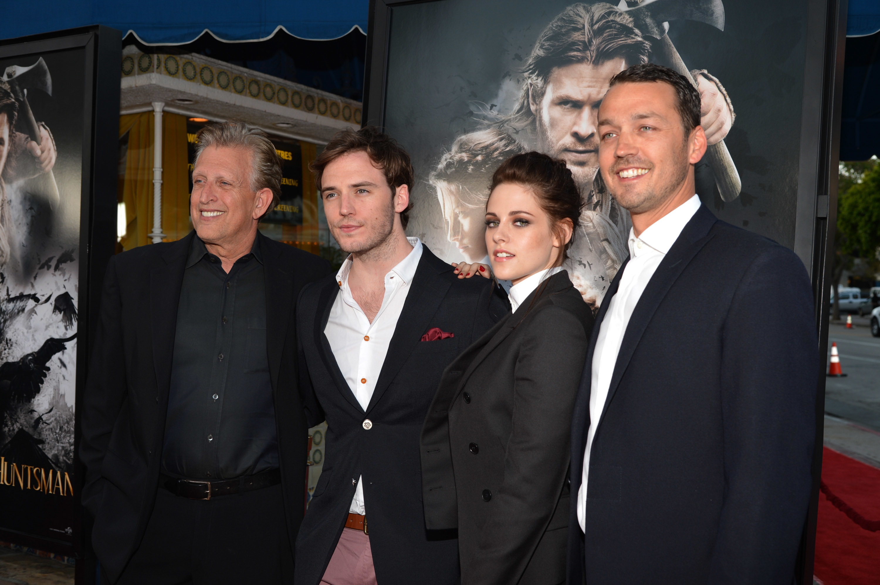 Four people in formal attire at a movie premiere, posed in front of a film poster