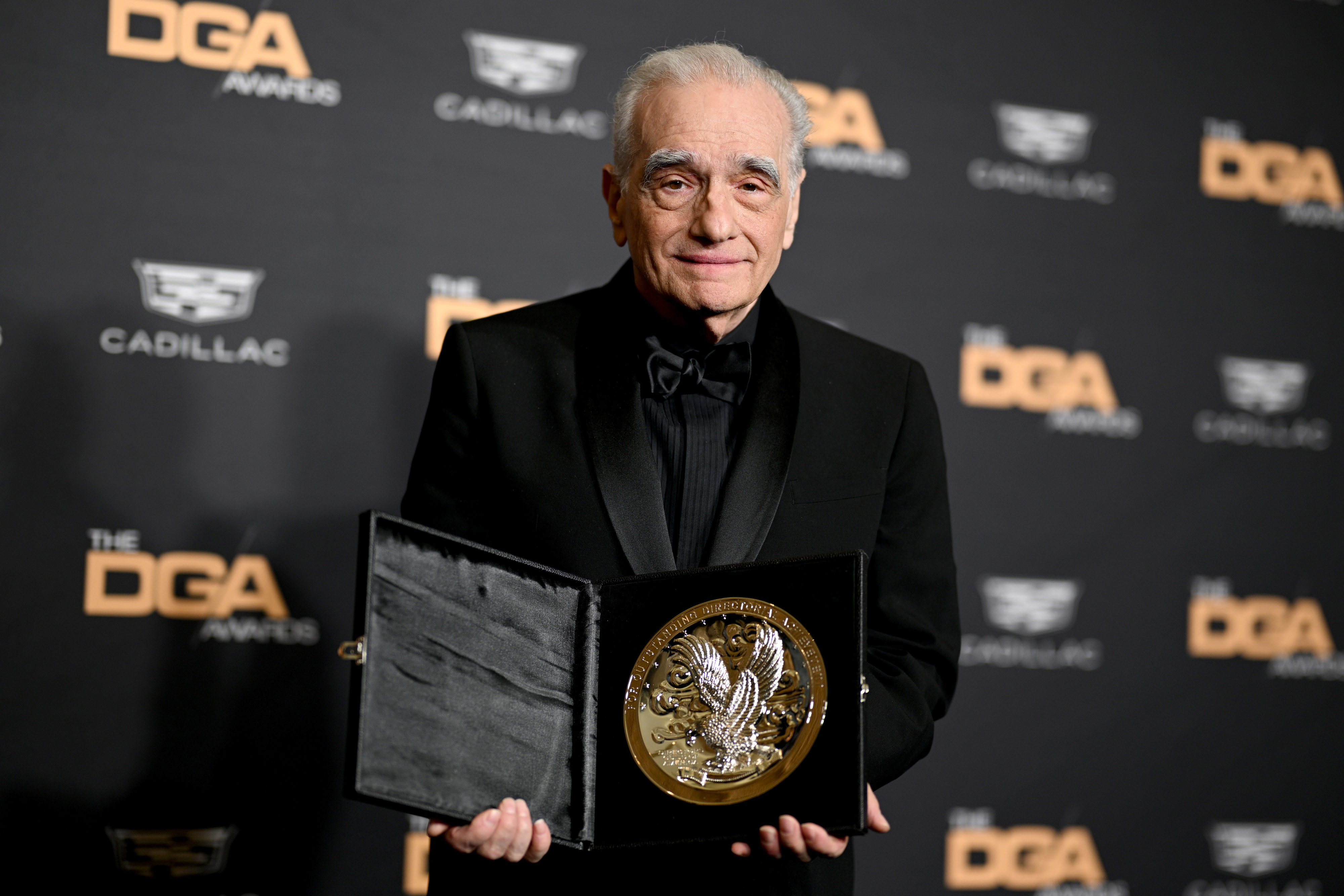 Person in a black suit holding a large award plaque at the DGA Awards