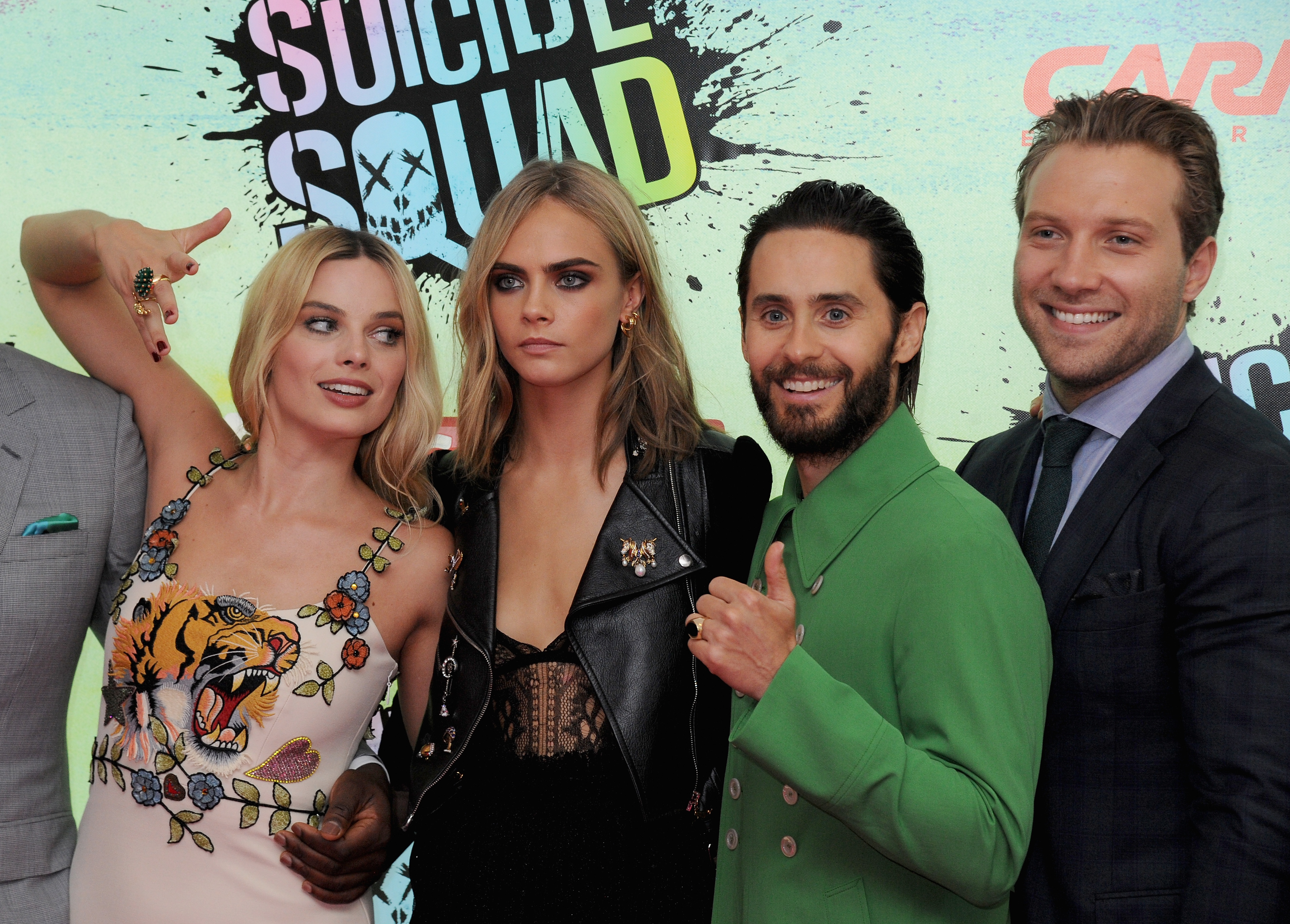 Group of four actors on a red carpet promoting &quot;Suicide Squad.&quot; One wears a floral dress, another a leather jacket, another a green suit