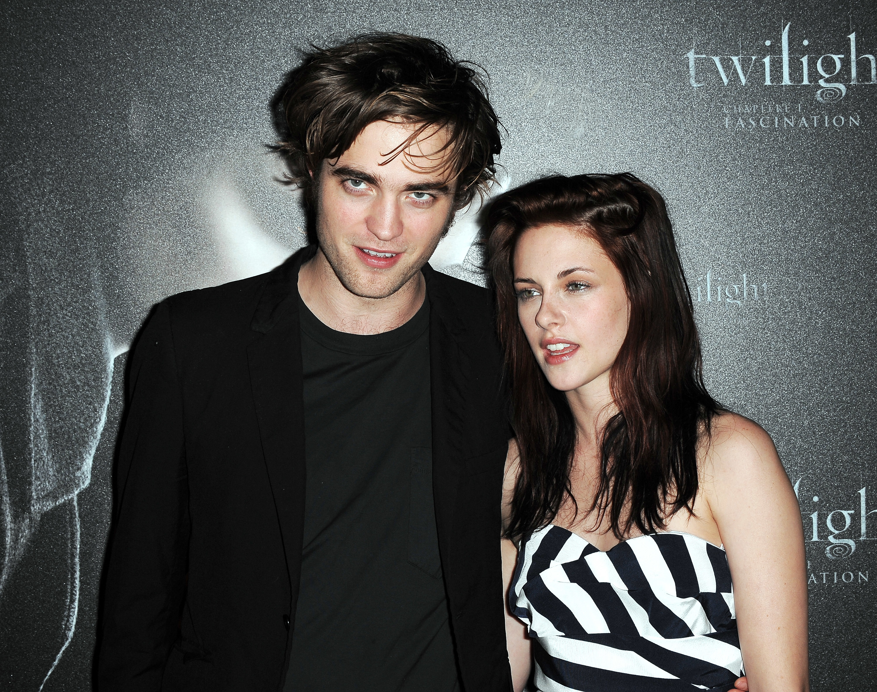 Two people pose at a &quot;Twilight&quot; event. One is in a dark suit, and the other is in a strapless dress with a geometric pattern