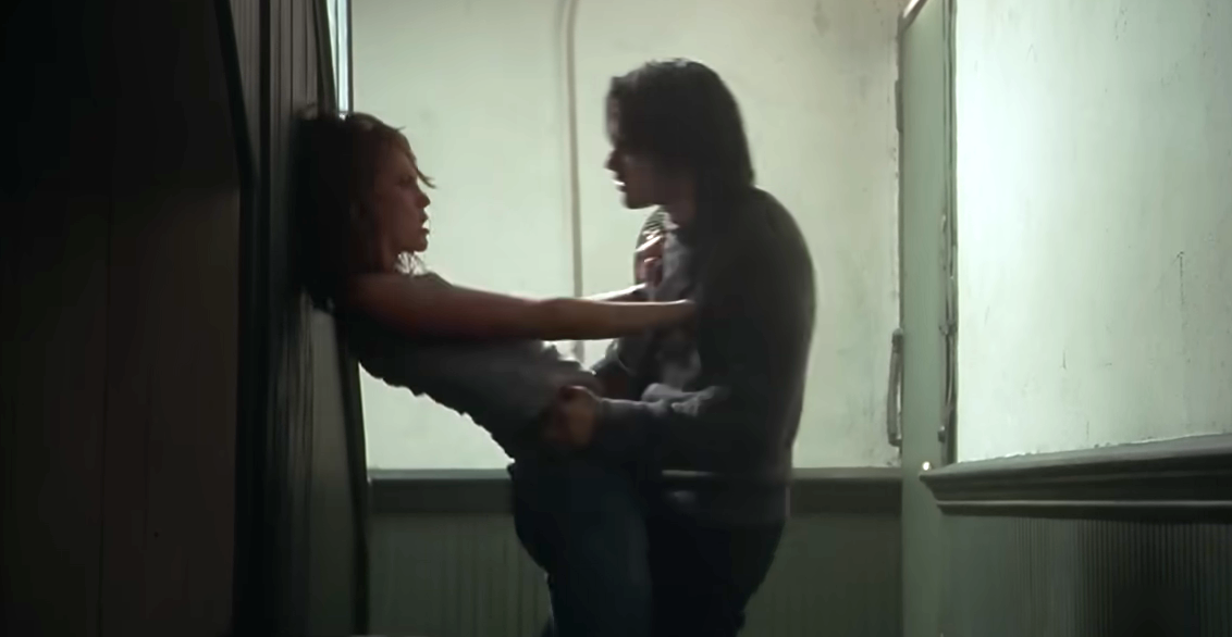 A scene from a movie shows a dramatic moment with a man pinning a woman against a wall in a hallway