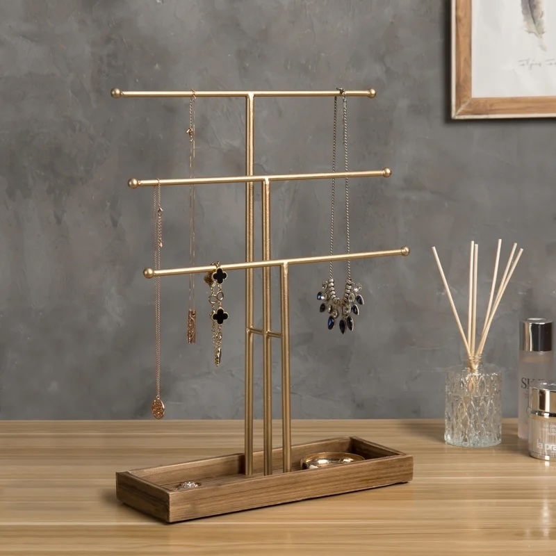 Jewelry stand on wooden base displaying necklaces. Perfume bottle and reed diffuser nearby on a table