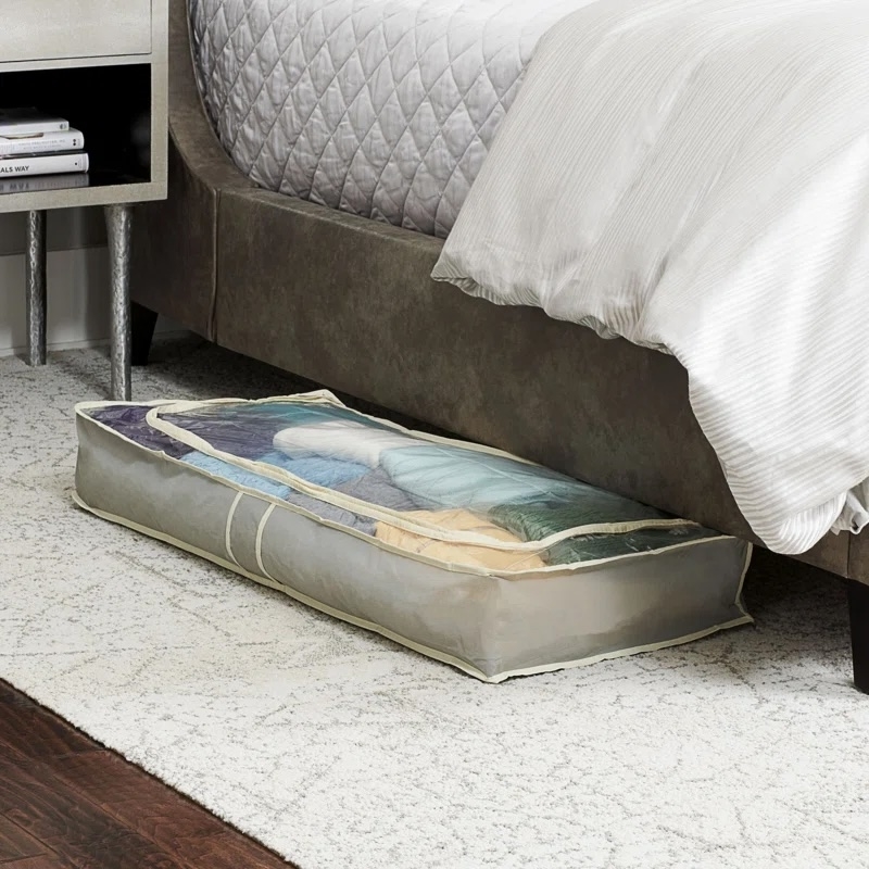 Under-bed storage bag with folded clothes, shown partially under a bed in a neatly organized bedroom setting