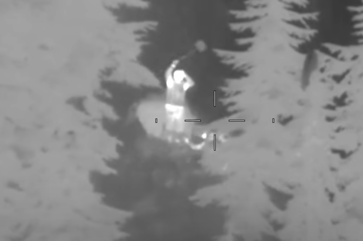 航空機から森林を監視する赤外線画像。人影が中央に浮かび上がる。テキストには左右の武装の表示が含まれる。