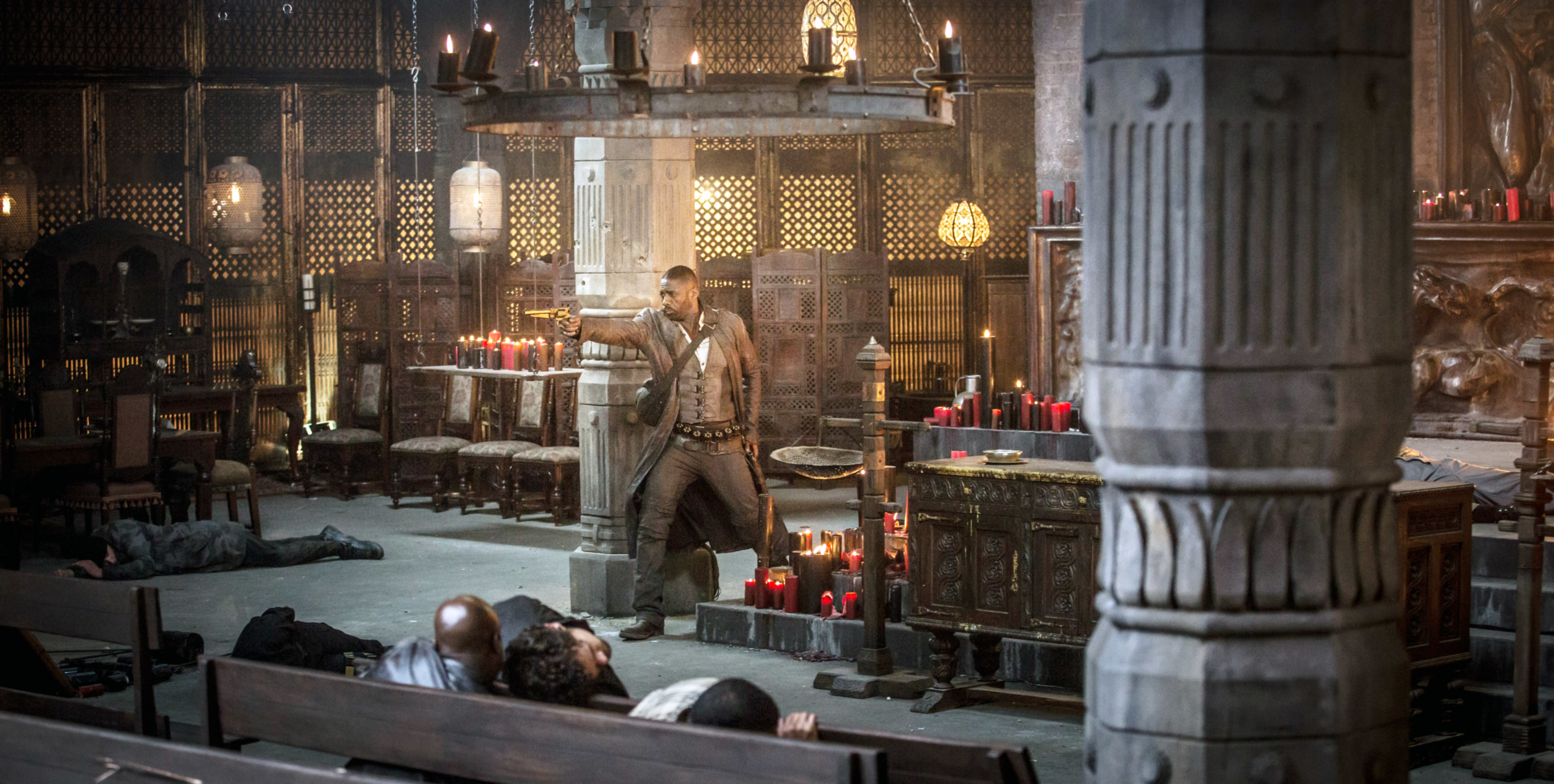 Scene from a dramatic film or show: a person aims a gun in an elaborately decorated room with candles and ornate furnishings