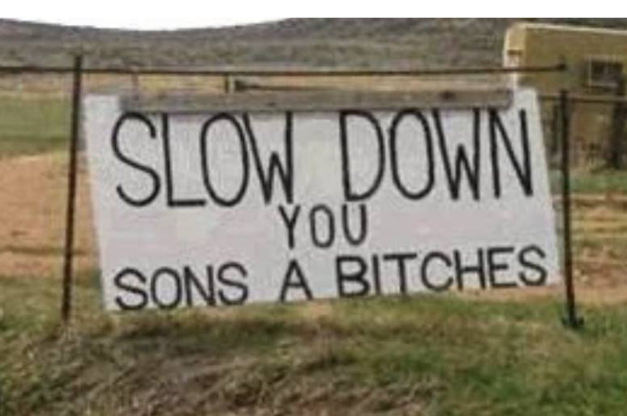 Sign reads: "SLOW DOWN YOU SONS A BITCHES" displayed outdoors on a fence