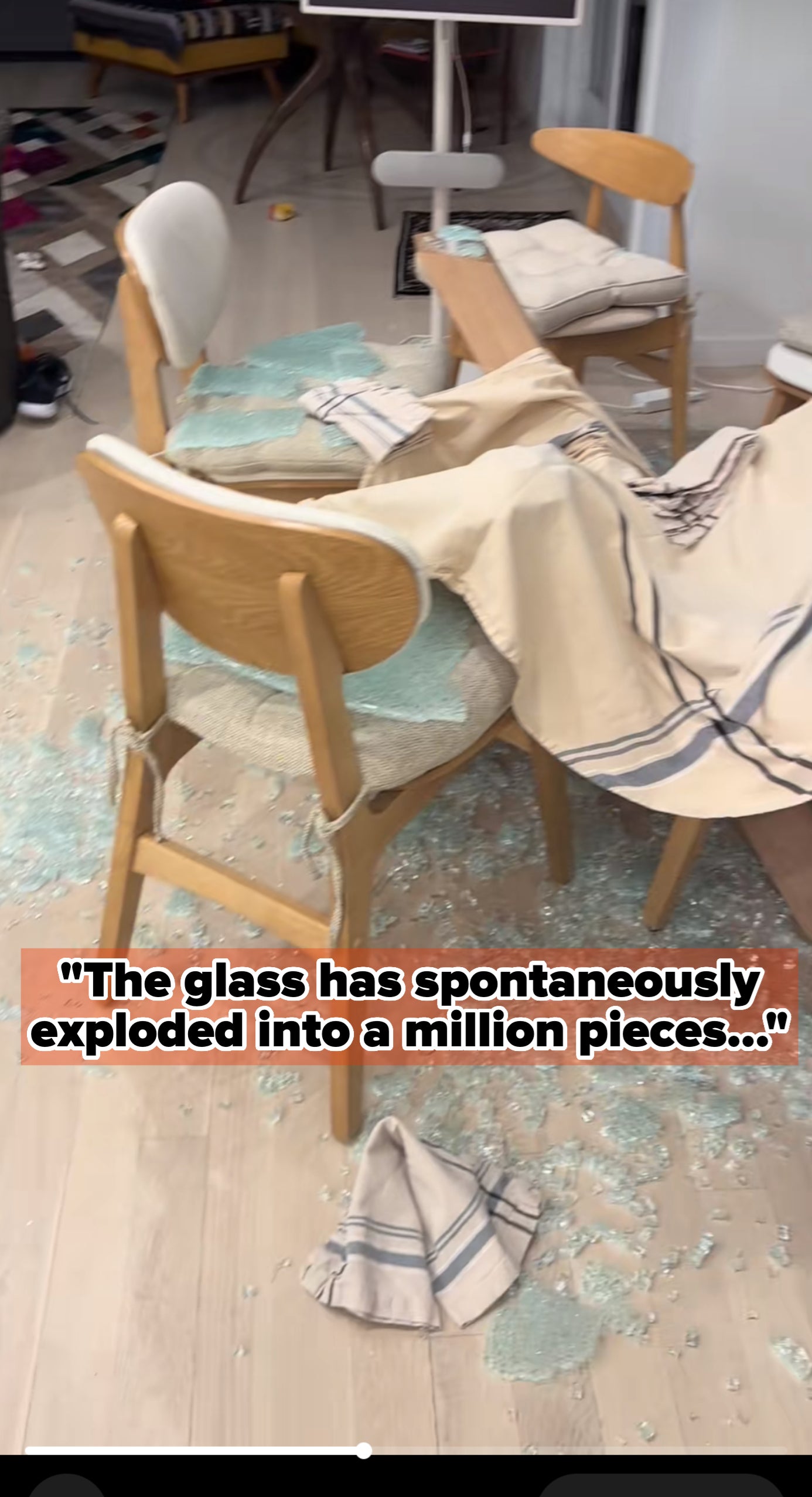 Shattered glass covers the floor beside a wooden chair, with a striped cloth draped over it in a room with furniture in the background. Captioned &quot;The glass has spontaneously exploded into a million pieces...&quot;