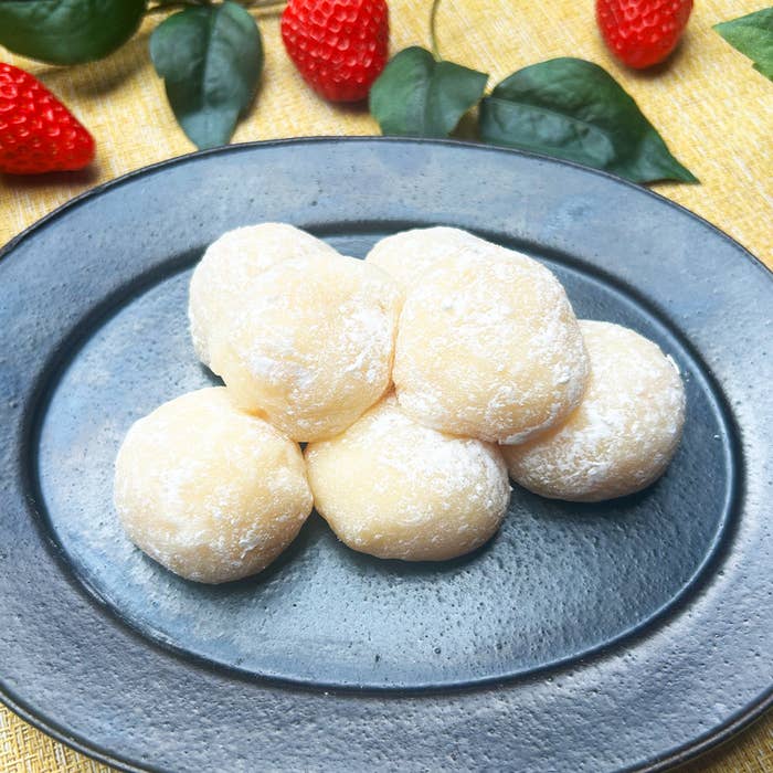 黒い皿に盛られた複数のもち、背景にいちごと葉。