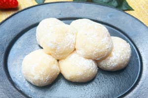 お皿に並んだいちごミルク餅と背後に飾られた新鮮ないちごと葉。