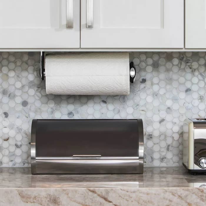Kitchen antagonistic  with stainless alloy  breadstuff  box, under-cabinet insubstantial  towel holder, and toaster against a tile backsplash