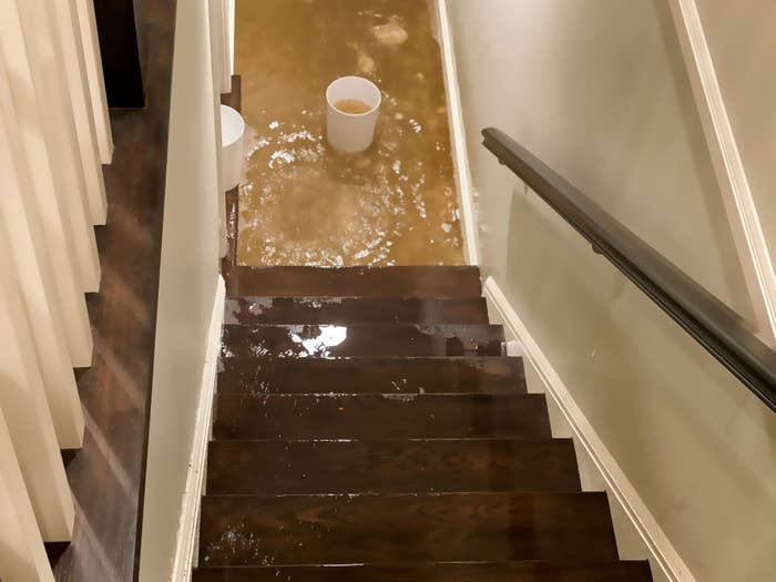 Flooded basement stairs with water pooling at the bottom; two buckets are placed for collecting the water