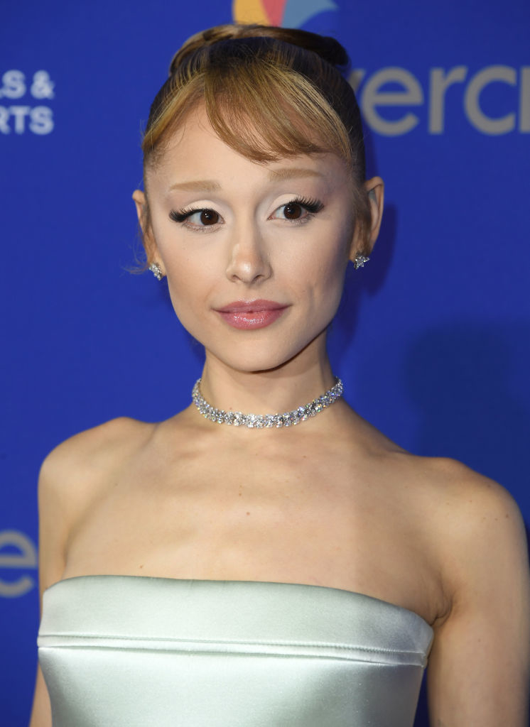 Person with an elegant updo hairstyle and a strapless, satin dress at a celebrity event, wearing a sparkling choker necklace