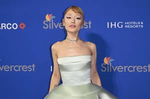 Person in elegant strapless dress on a red carpet, posing in front of a backdrop with logos