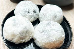 黒い皿の上に4つの餅菓子が載っている。背景に茶碗が見える。