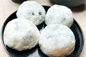 黒い皿の上に4つの餅菓子が載っている。背景に茶碗が見える。