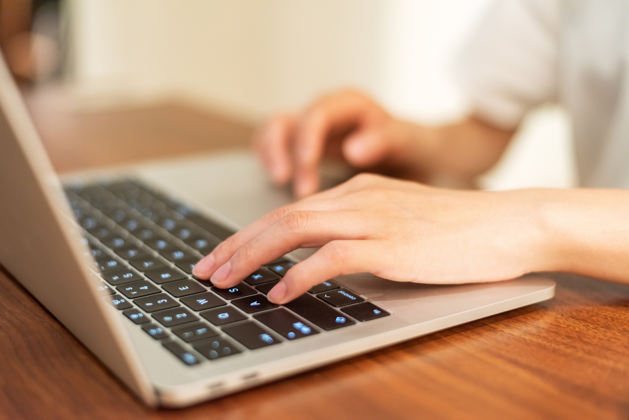 A person types on a laptop, focusing on the keyboard, with hands visible on a wooden table